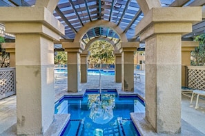 An outdoor swimming pool with a clear view of the surrounding area, including a covered seating area and a poolside fence.
