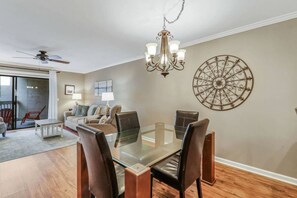 A dining area with a glass table, leather chairs, a chandelier, and a decorative wall piece.