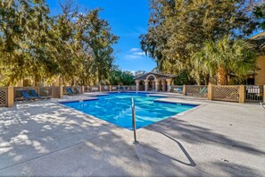 A rectangular swimming pool with a diving board, surrounded by lounge chairs and a covered pavilion.