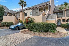 A residential building with a paved driveway, a parked car, and a well-maintained garden with a palm tree.