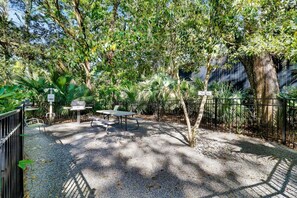 An outdoor seating area with a picnic table and chairs, surrounded by a fence and lush greenery.