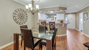 A dining area with a glass table and chairs, a chandelier, and a decorative wall piece. - 145 Colonnade Club Villa Beach Path, Pool, Hot Tub (Hilton Head Island)
