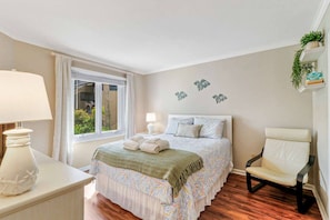 A bedroom with a bed, bedside lamps, a chair, a window with curtains, and a wall with decorative elements.