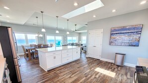 A spacious kitchen with wooden flooring, white cabinetry, and pendant lighting. - Mermaid Cove – Splash Into Relaxation (North Topsail Beach)