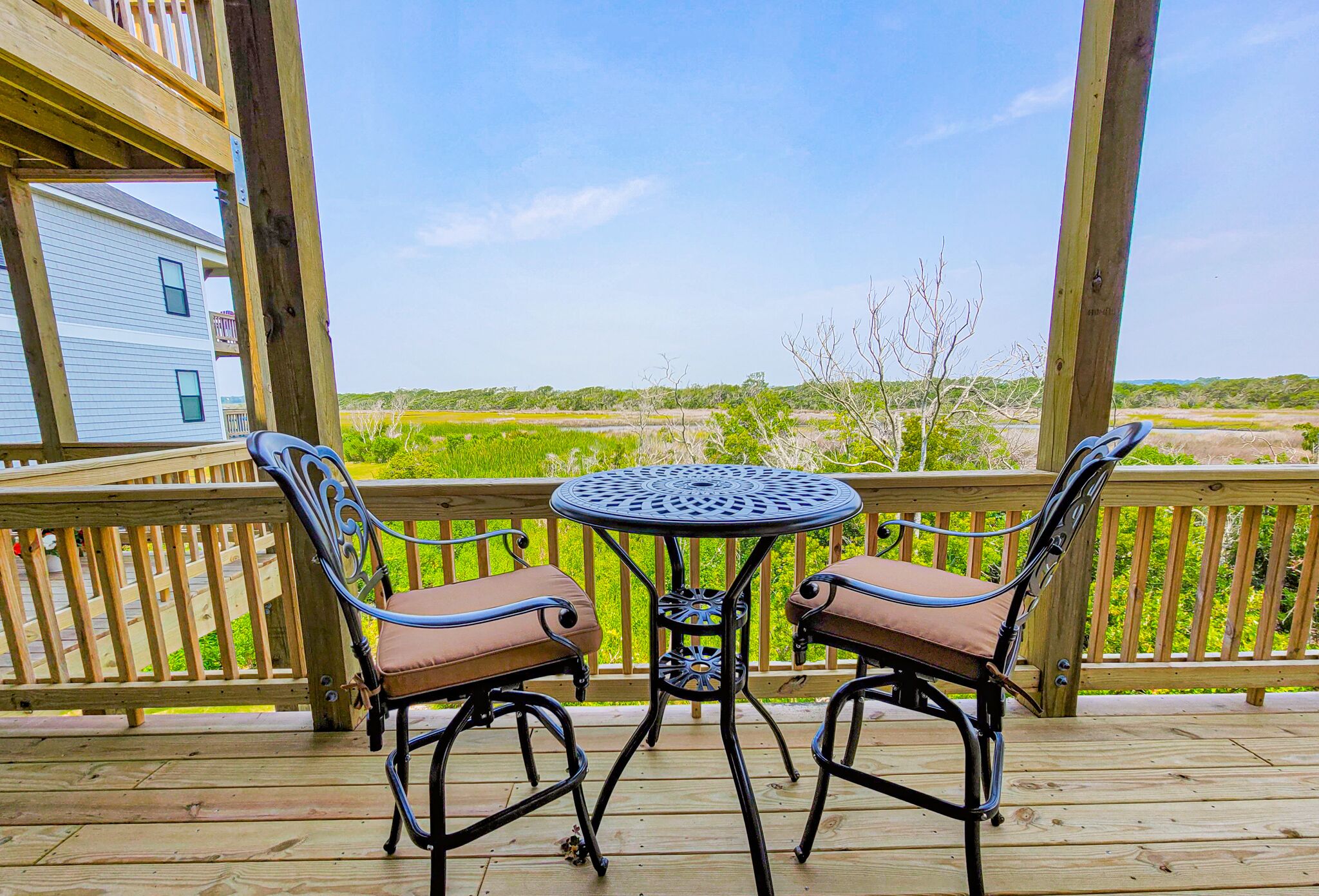 Een houten terras met twee metalen stoelen en een tafel, met uitzicht op een groen landschap.