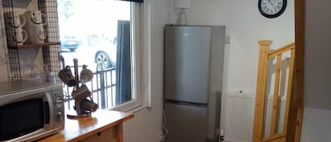 A compact kitchen with a microwave, refrigerator, and wooden table.