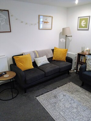 A living room with a sofa, a lamp, a radiator, and a small table with a remote control. - Close to the Seaside - Sleeps 4/free Wifi/parking (Leven)
