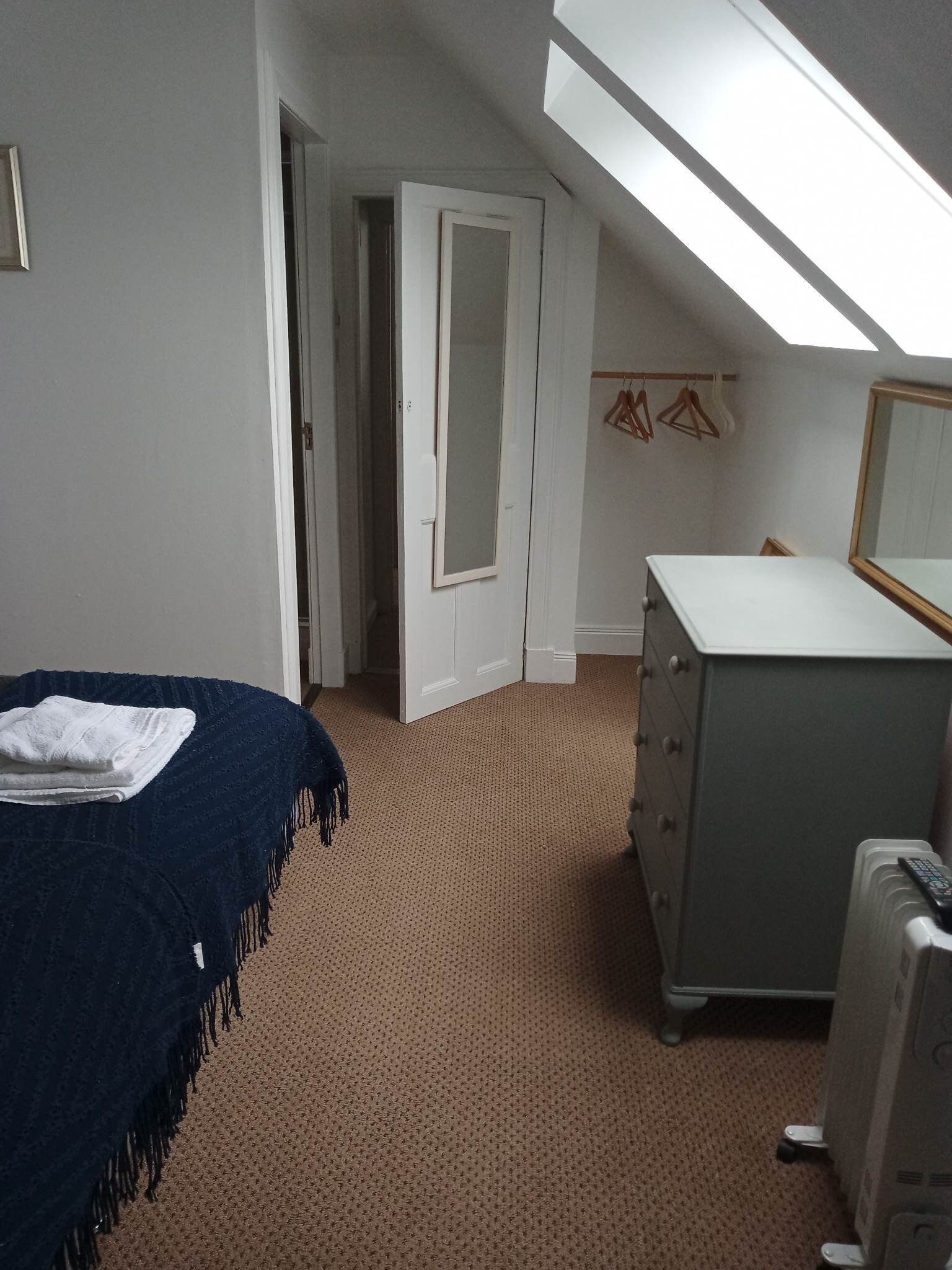 Un dormitorio con una cama, un aparador, un espejo y una puerta que da a otra habitación.