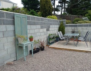A patio area with a table and chairs, surrounded by a stone wall and potted plants. - Seaside Escape in Lundin Links (Leven)