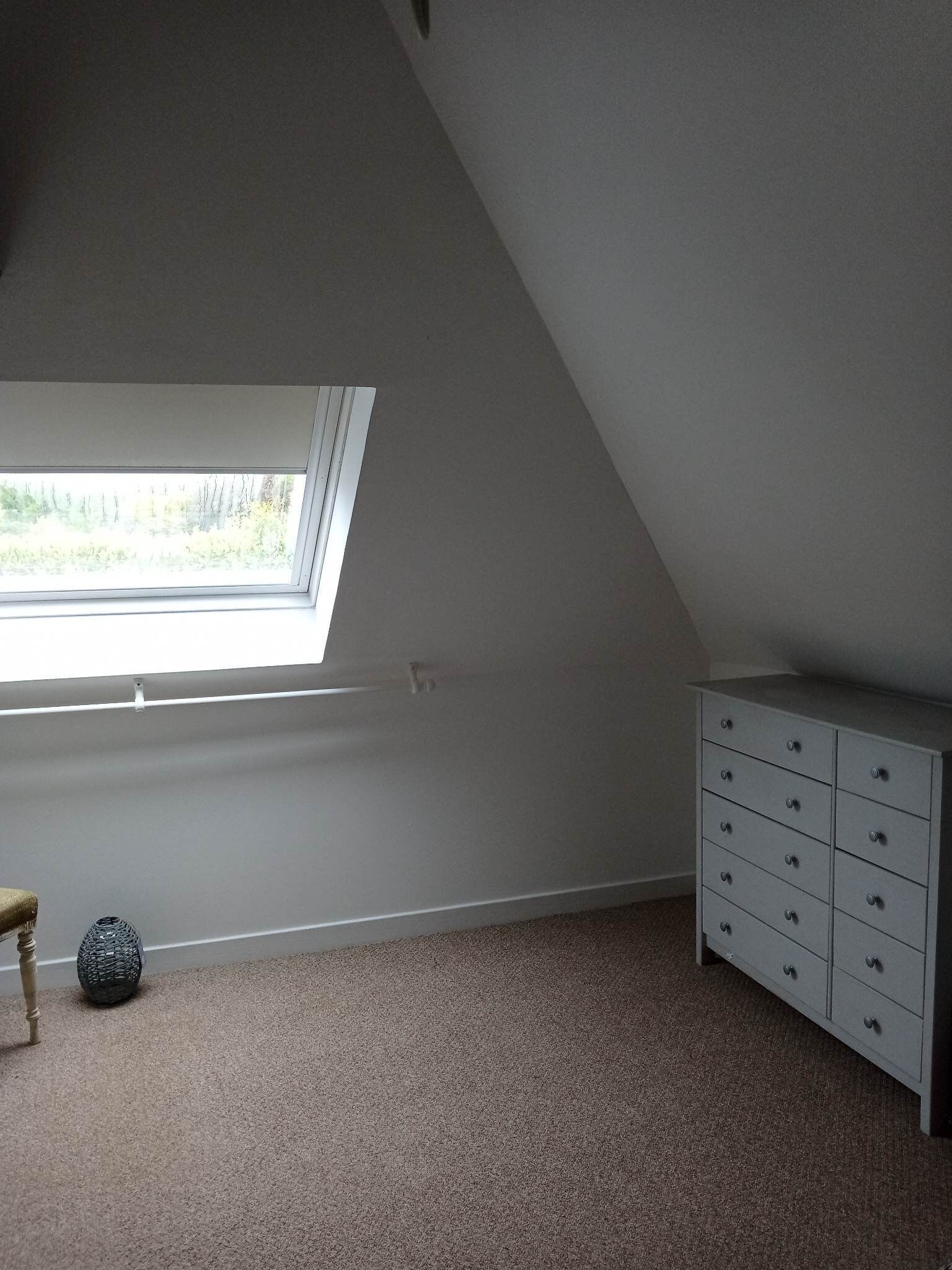 Ein Zimmer mit schrägem Dach, einem Fenster, einem Schminktisch und einem kleinen runden Tisch.