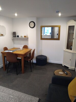 A dining area with a wooden table and chairs, a clock on the wall, a mirror, and a cabinet. - Close to the Seaside - Sleeps 4/free Wifi/parking (Leven)