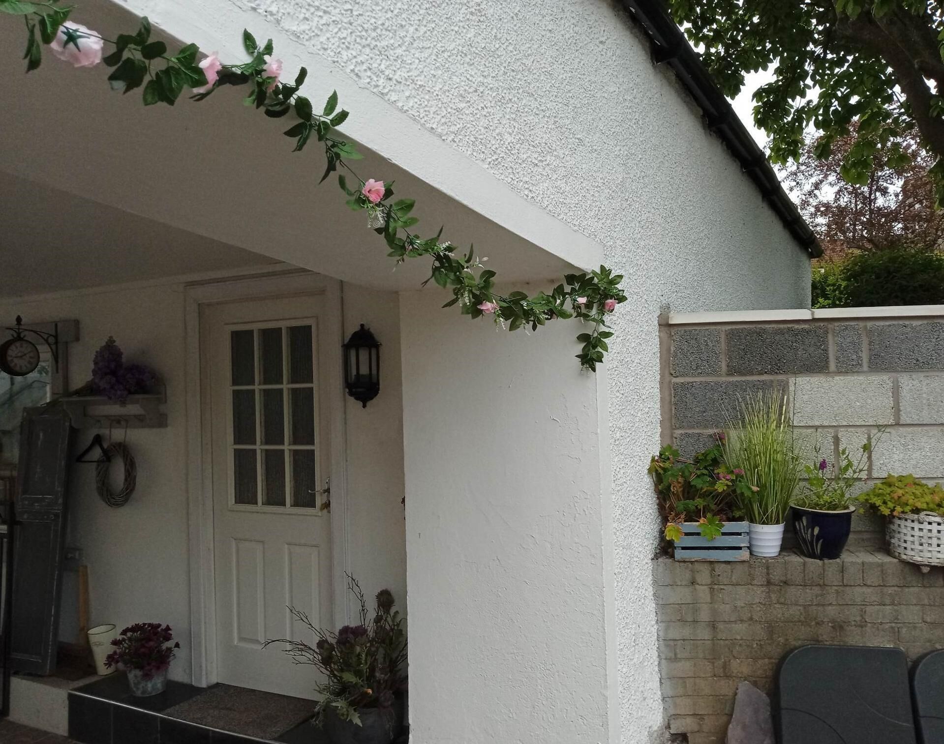 Une façade blanche avec une porte, un petit espace de porche et un jardinier mural contenant diverses plantes.