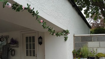 Une façade blanche avec une porte, un petit espace de porche et un jardinier mural contenant diverses plantes.