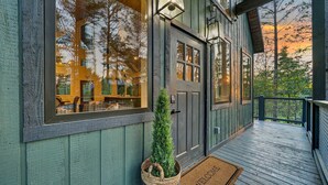 A wooden house with a porch, a welcome mat, and a small tree in a basket. - Luxury Treehouse! Elevated, Magical & Unique! (Broken Bow)
