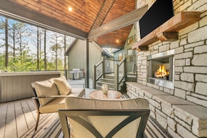 Un espacio al aire libre acogedor con chimenea de piedra, terraza de madera y una escalera que conduce a un nivel superior.