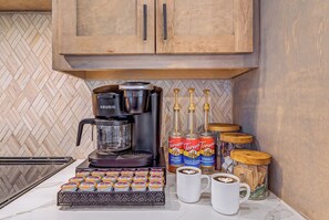 Una cocina con cafetera, botellas de sirope Torani y una bandeja de alimentos envasados.
