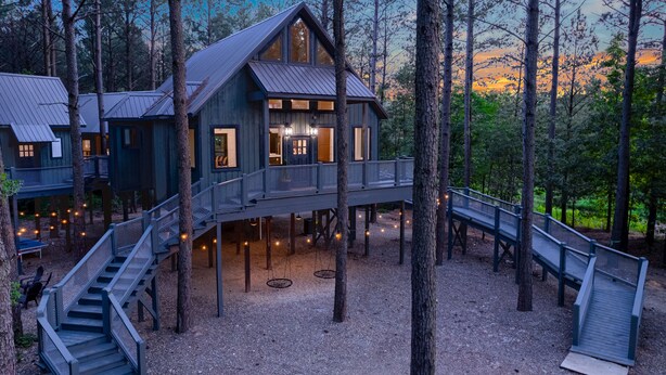 A cabin with a deck and stairs, surrounded by trees. - Luxury Treehouse! Elevated, Magical & Unique! (Broken Bow)