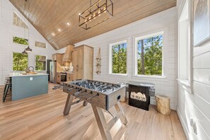 A spacious kitchen with a foosball table, wooden cabinets, and large windows.