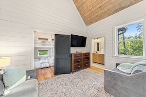 A room with a bed, a dresser, a television, and a window with a view of greenery. - Magical Luxury Treehouse! Epic Play Area! Bowling! (Broken Bow)