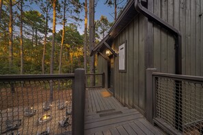 A wooden cabin with a deck, surrounded by trees.