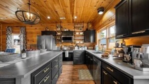 A modern kitchen with wooden walls, a large island, and stainless steel appliances. - 🍃Serendipity Lodge🌲Mountain Views, Theater, Game Room & Pet-Friendly (Sevierville)