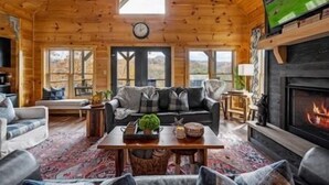 A cozy log cabin interior with a fireplace, a sofa set, and a large TV screen. - 🍃Serendipity Lodge🌲Mountain Views, Theater, Game Room & Pet-Friendly (Sevierville)