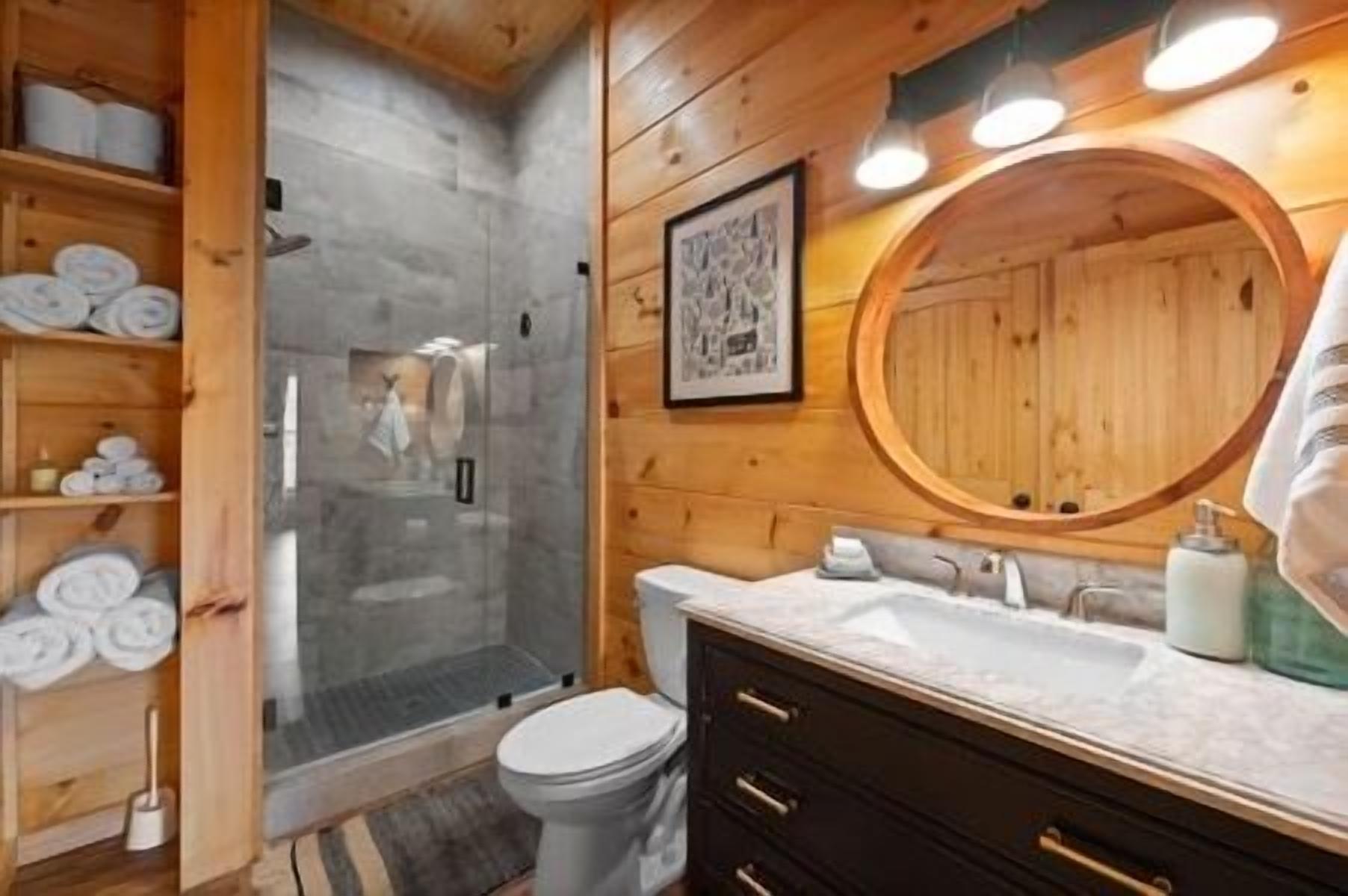 Bagno di una cabina in legno con box doccia in vetro, un water, un mobile lavabo e uno specchio grande.