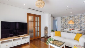 Un salon moderne doté d’un téléviseur à écran plat, d’un meuble de rangement en bois, d’un canapé blanc agrémenté de coussins jaunes et d’un mur à motifs.