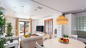 Un salon moderne avec un canapé, une table à manger et des chaises. On y trouve également un téléviseur et une fenêtre avec des rideaux.