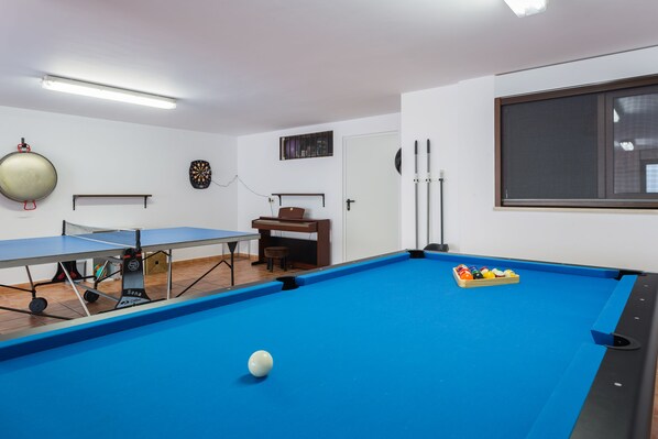 Una habitación con mesa de billar azul, mesa de ping pong y dardos.