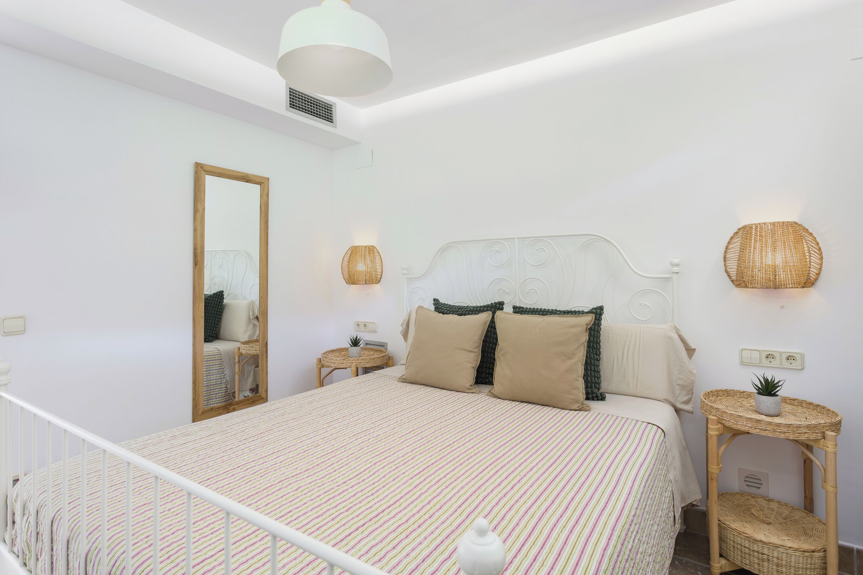 Ein Schlafzimmer mit einem Bett, Nachttischen, einem Spiegel und einer Wandlampe.