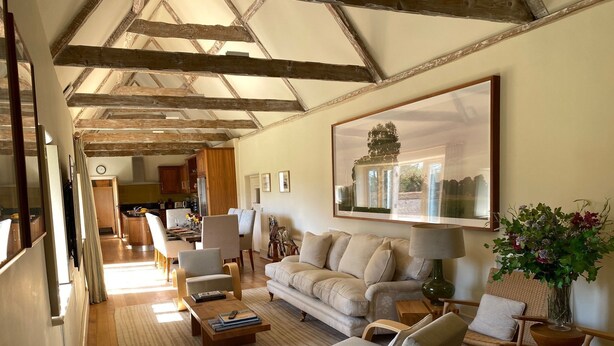 A spacious living area with a high ceiling, wooden beams, a large painting, and a cozy seating arrangement. - The Barn (Hunstanton)