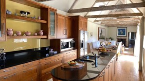 A kitchen with wooden cabinets, a black countertop, and a central island with a sink. - The Barn (Hunstanton)