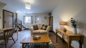 Una sala de estar acogedora con una mesa de madera, un sofá y una escalera que lleva a otra habitación.