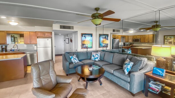 A modern living room with a sofa, chairs, and a coffee table. There is a kitchen in the background with cabinets and appliances. - Ma'alaea Surf #G-2 – Relaxing Ground-Floor Getaway (Kihei, Maui)
