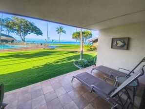 A patio with a view of a well-maintained lawn, a swimming pool, and a building with a framed picture on the wall.