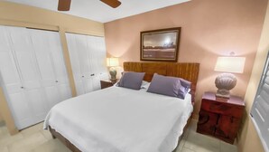 A bedroom with a bed, two nightstands, a ceiling fan, a framed picture on the wall, and a door. - Ma'alaea Surf #G-2 – Relaxing Ground-Floor Getaway (Kihei, Maui)