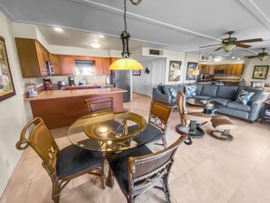 Une cuisine moderne dotée d’un îlot central, un coin repas avec une table ronde et des chaises, et un salon avec un canapé et une table basse.