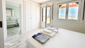 Een slaapkamer met een bed, een badkamer met een spiegel, en uitzicht op zee door een raam.