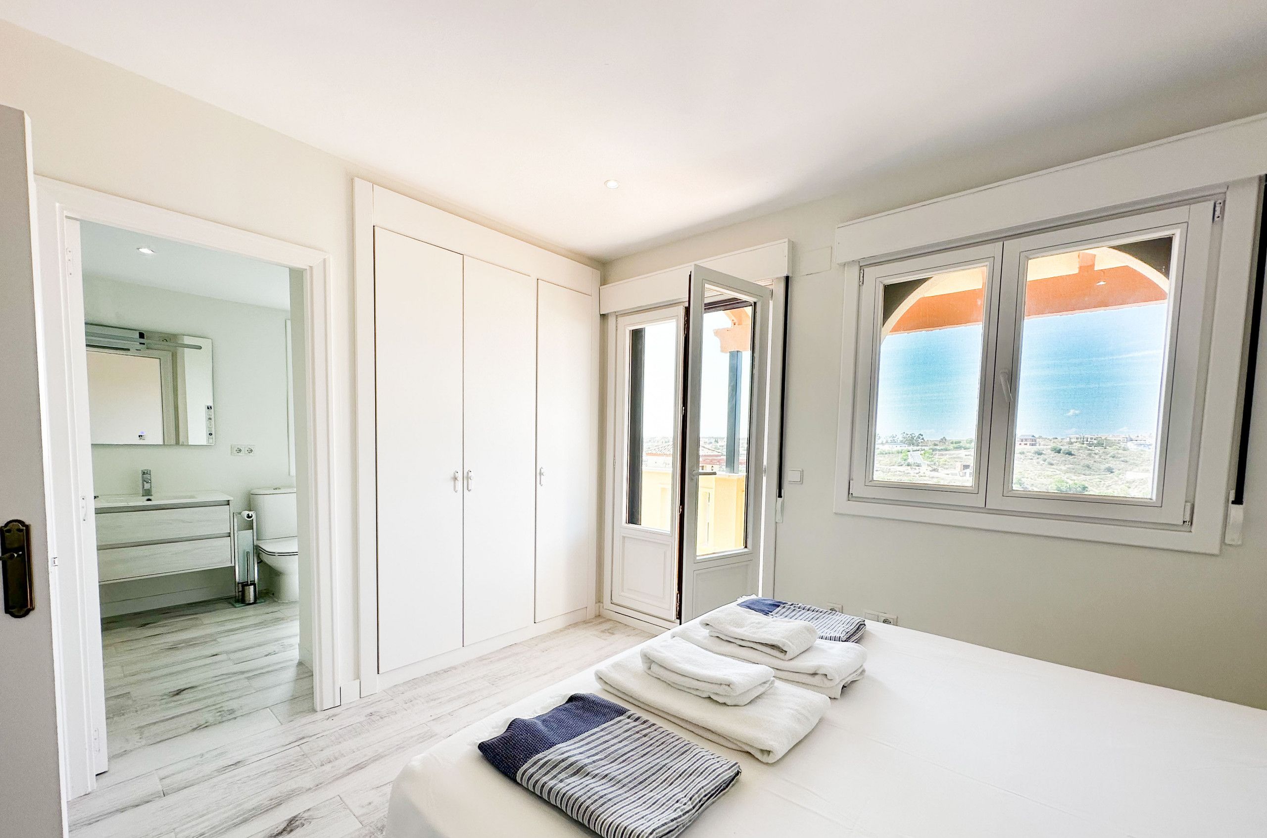 A bedroom with a bed, a bathroom with a mirror, and a view of the sea through a window.