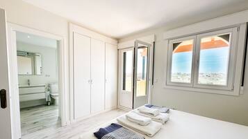 A bedroom with a bed, a bathroom with a mirror, and a view of the sea through a window.