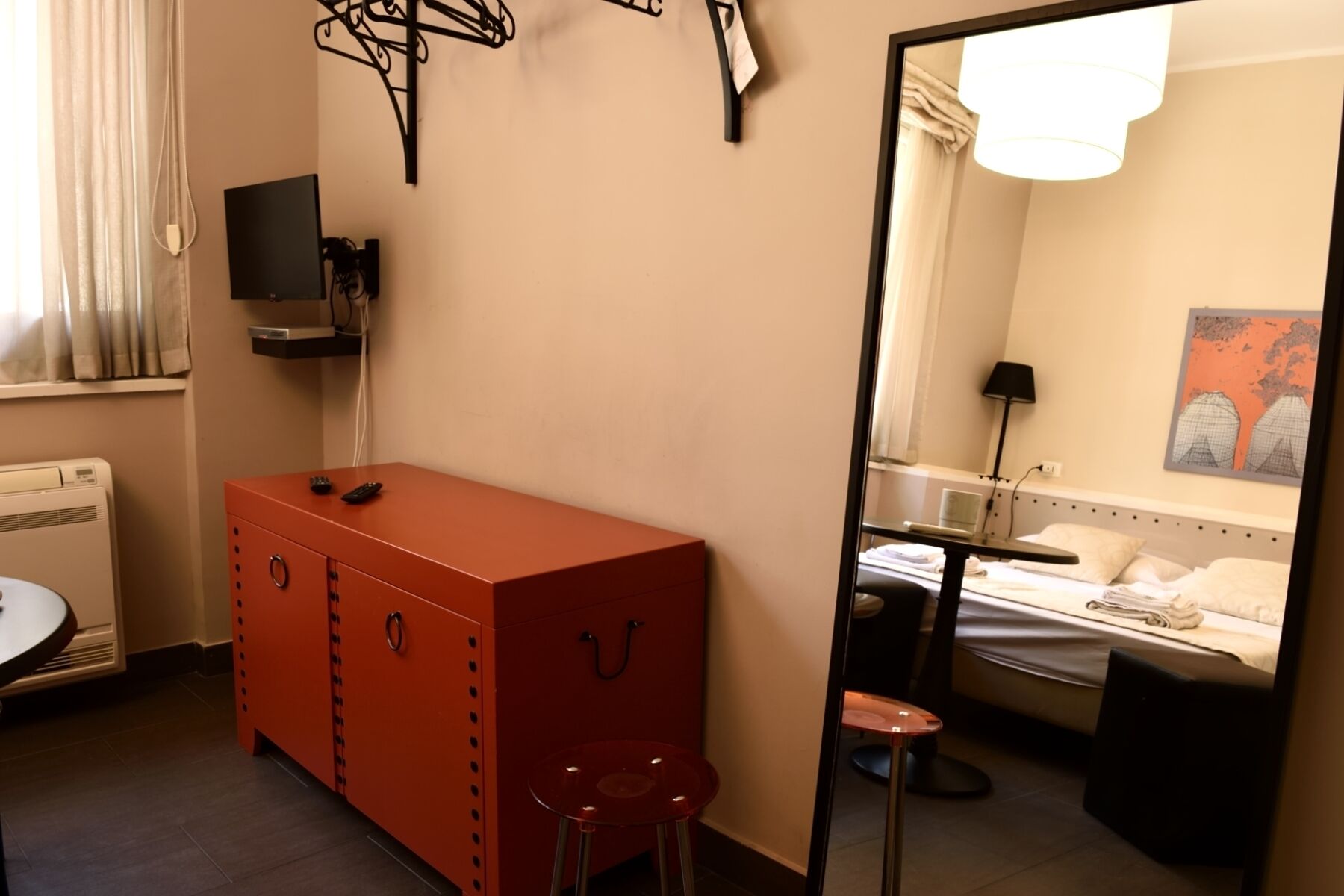 Una habitación de hotel con una cama, un escritorio, un espejo y un armario rojo.
