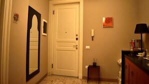 En hall med en vit dörr, ett litet bord med en lampa och en spegel på väggen.