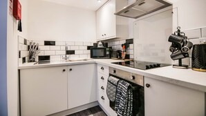 A modern kitchen with white cabinets, a black and white tiled backsplash, a microwave, a stove, and a coffee maker. - Apartment 1 - The Crescent (York)