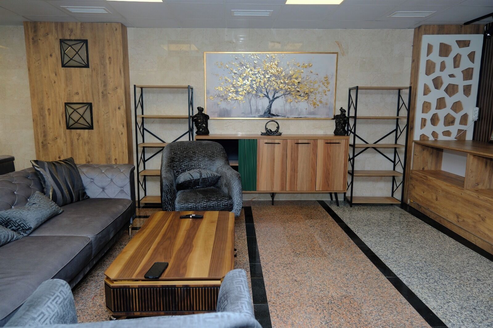 A modern living room with a grey sofa, a patterned armchair, a wooden coffee table, and a painting of a tree.