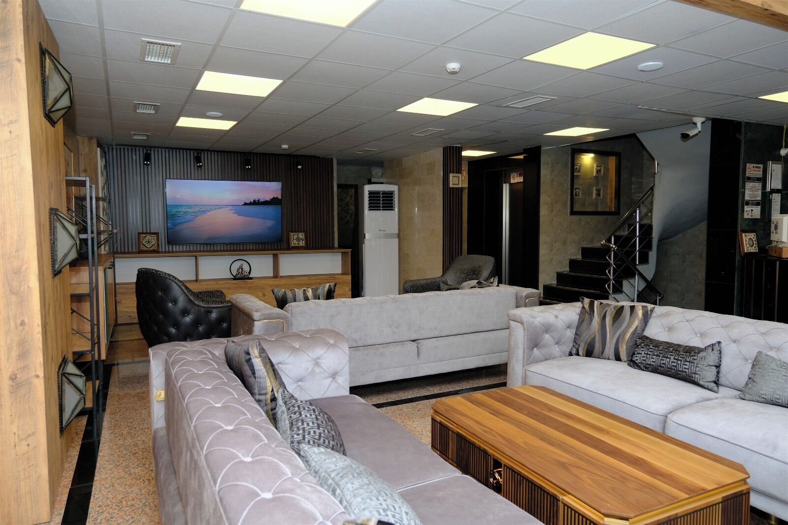 A modern living room with a large flat-screen TV, a staircase, and a wooden coffee table.