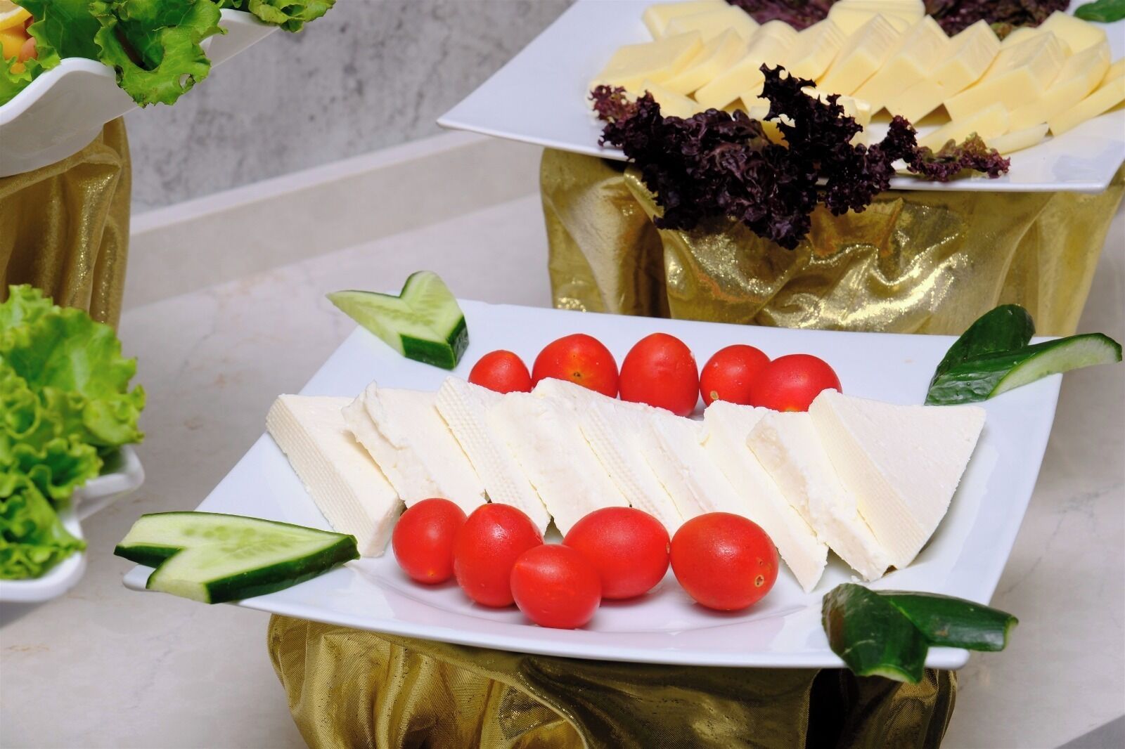 A buffet table with various food items including cheese, tomatoes, and leafy greens.