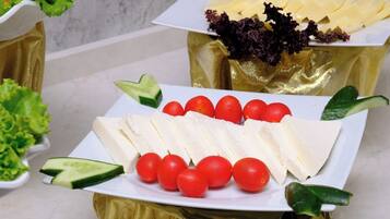 A buffet table with various food items including cheese, tomatoes, and leafy greens.