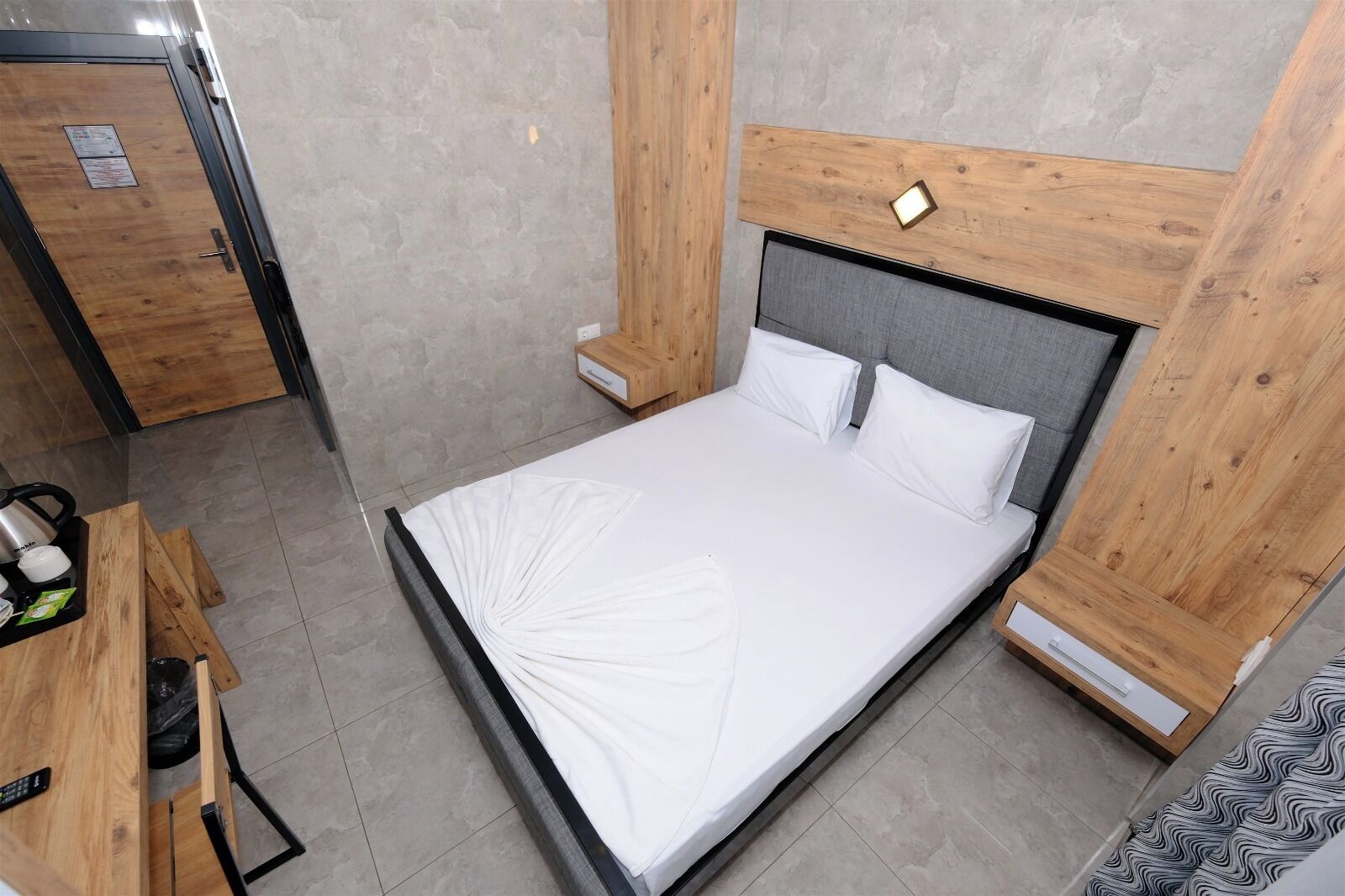 Un lit simple avec une tête de lit en bois et des tables de chevet, un bureau en bois avec une chaise, et un tapis à motifs.