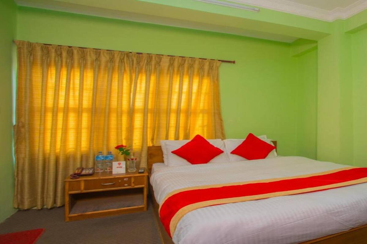 A hotel room with a bed, a nightstand, a lamp, and a window with curtains.